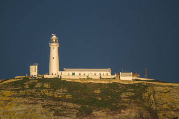 Fototapeta na wymiar Lighthouse on rocky outcrop in morning light, copyspace