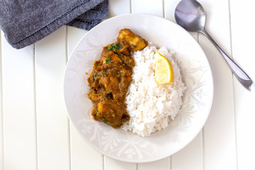 Close up traditional Indian butter chicken curry and lemon served with boiled rice white plate. Top view.