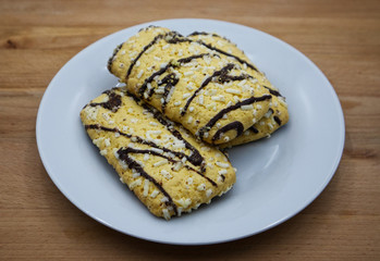 Cookies with chocolate glaze and sugar crystals on white dish, wooden table