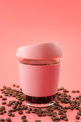 Coffee break, a shot of caffeine and energy in a cup of java concept theme with a reusable portable glass hot beverage mug surrounded by fresh beans isolated on pink background