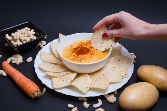 Queso chedar vegano con piment&oacute;n y con nachos para mojar, hecho con patatas, zanahoria y anacardos, sobre fondo negro.