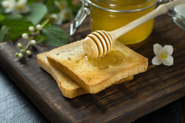 wooden spoon with honey is lying on a piece of bread near a glass jar of honey