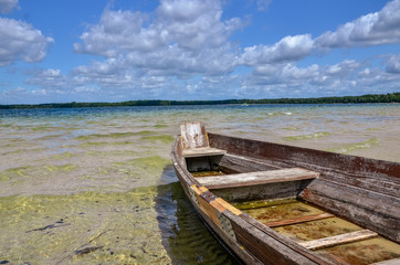 Rustic wooden fishing boat on the lake with transparent blue sky and clear water