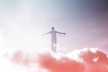 Silhouette of a man flying up in the sky in the bright rays of the sun with arms spread apart.