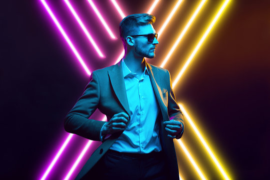 Young handsome model posing in a studio in a trendy neon light. Fashionable man in a stylish suit. Vibrant color. Bright colorful light effects. Disco style. Overlay. Gel filter. Supersaturated