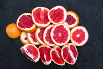 Ripe juicy cut red grapefruit slices on black wood background closeup