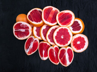 Ripe juicy cut red grapefruit slices on black wood background closeup