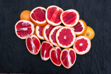Ripe juicy cut red grapefruit slices on black wood background closeup