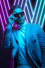 Young handsome model posing in a studio in a trendy neon light. Fashionable man in a stylish suit. Vibrant color. Bright colorful light effects. Disco style. Overlay. Gel filter. Supersaturated