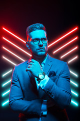 Young handsome model posing in a studio in a trendy neon light. Fashionable man in a stylish suit. Vibrant color. Bright colorful light effects. Disco style. Overlay. Gel filter. Supersaturated