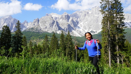 Naklejka premium fröhliche asiatische Touristin wandert durch hohes Gras in den Dolomiten in Südtirol