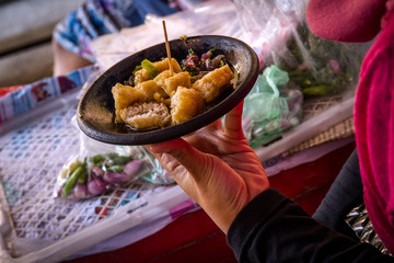 A woman enjoys traditional food fried tofu mixed crushed chilli, garlic, shallot and sauce in the market