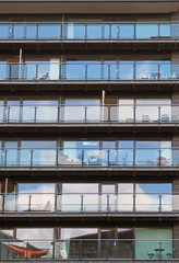 Obraz premium rows of apartments in a large modern building with glass balconies and outdoor furniture and sky reflected in the windows