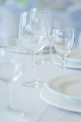 Clean empty glasses and plates on the table in the restaurant prepared for guests. 