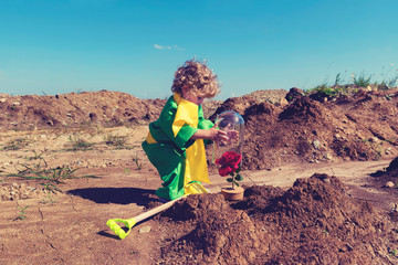 Cute blond toddler boy covers red rose with glass lid in the desert  Little prince concept...