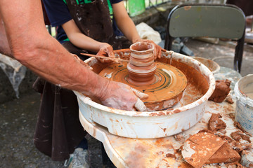 Close up pottery. Adult potter muddy hands guiding child hands to help with clay on a wheel. Child trying to make a simple clay pot or plate