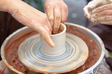 Fototapeta na wymiar Close up pottery. Adult potter muddy hands guiding child hands to help with clay on a wheel