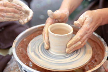 Fototapeta na wymiar Close up pottery. Adult potter muddy hands guiding child hands to help with clay on a wheel