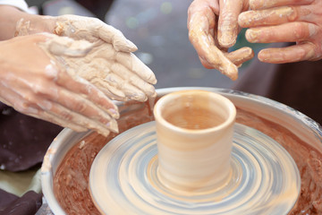Close up pottery. Selective focus. Adult potter muddy hands guiding child hands to help with clay on a wheel