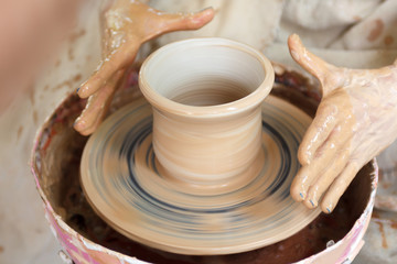 Close up pottery. Selective focus. Adult potter muddy hands guiding students hands to help with clay on a wheel