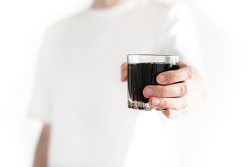 Man gives a glass of cola to camera isolated on a white background. Dark fizzy soda. Soda black in...
