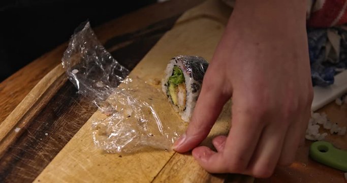 Close view hands holding California Maki sushi in folie. Prepering sushi.