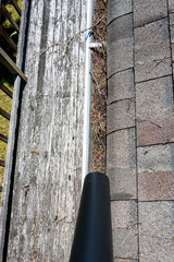 View from rooftop of leaf blower tube, asphalt roof shingles and gutter filled with tree debris, deck and back yard below, time for gutter cleaning