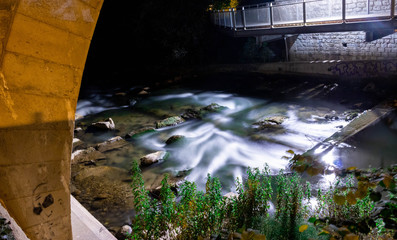 Long exposure capture of a river following over some rocks through a bridge 