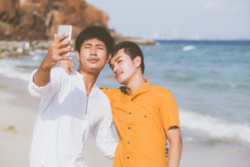 Gay portrait young couple smiling taking a selfie photo together with smart mobile phone at beach, LGBT homosexual lover in the vacation at sea, two man going to travel, holiday concept.