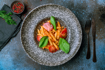 Pasta Penne arabiata on grey plate on blue concrete table
