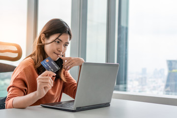 Young asian woman holding mockup credit card and use laptop for purchase product on internet in home office, Cyber Monday shopping online concept, Copy space.
