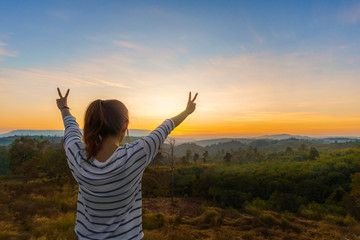 Asian woman standing and hand up in tropical forest and looking far away at sunrise time.