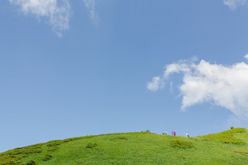 Obraz premium Peopple standing on the green hill on skyline in the summer day, blue sky, white clouds. Day light. Horizontal image.