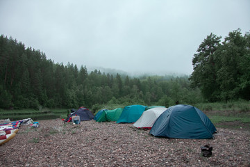 Camping tents on the beach. Tourists rafting on the river on a halt