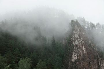 Mountain landscape with rocks and creeping fog. High peaks in the clouds, cold weather. Tourism in the mountains