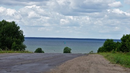 road and water of lake at sunny day by cloudy sky