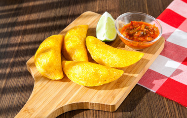 Colombian empanada with spicy sauce on wooden background