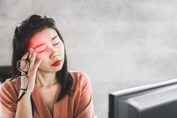 Asian woman worker suffering from eye pain working on computer screen, hand holding eyeglasses 