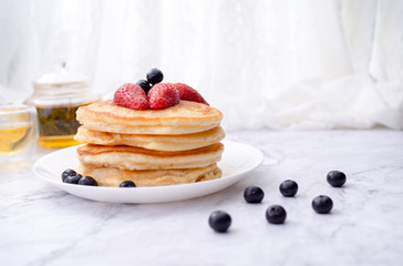 Stack of pancakes with topping, strawberry and blueberry.Placed in a white plate on a marble table and copy space.Eat with tea in the glass.