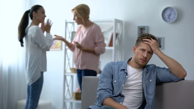 Exhausted male listening wife and mother-in-law arguing at home, rivalry