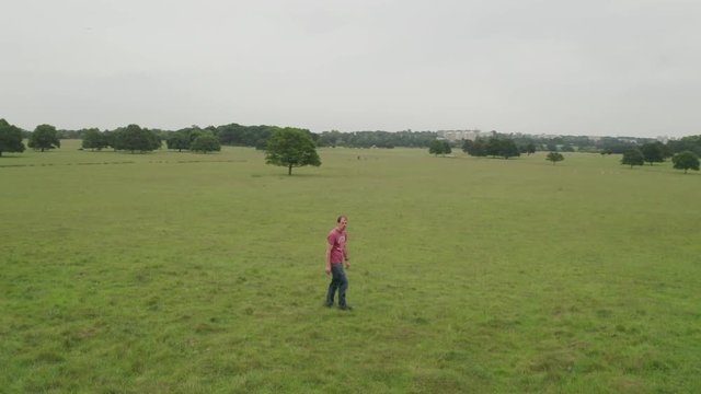 Aerial shot of a man walking in a green open space, camera rotates round while walking.