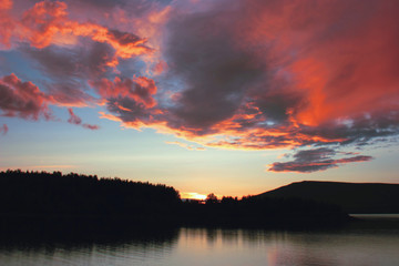 Obraz premium yellow and pink clouds at sunset over a mountain lake
