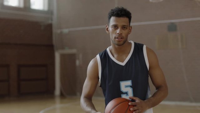 CU Portrait of young confident African American black college basketball player in generic uniform posing with a ball, looking into camera. Shot on ARRI Alexa Mini, 4K RAW graded footage