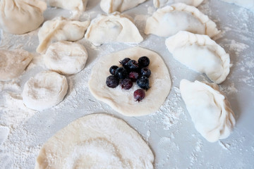 Sculpted dumplings with Irga, raw dough. Stages of preparation of sweet flour boiled dishes. White table with flour and roll the dough.