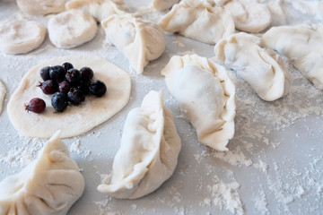 Sculpted dumplings with Irga, raw dough. Stages of preparation of sweet flour boiled dishes. White table with flour and roll the dough.
