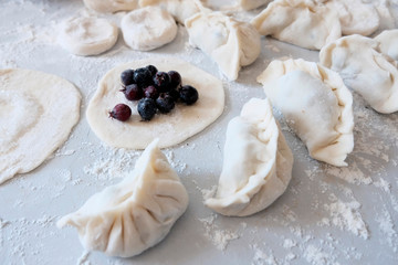 Fototapeta na wymiar Sculpted dumplings with Irga, raw dough. Stages of preparation of sweet flour boiled dishes. White table with flour and roll the dough.