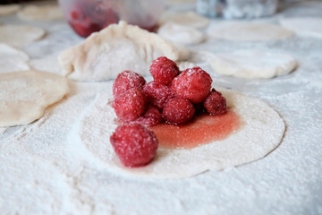 The concept of cooking dough. The rolled out circle of dough with filling in the middle of the strawberries. The background of scattered flour, raw pieces of dough next.Dumplings with berries.