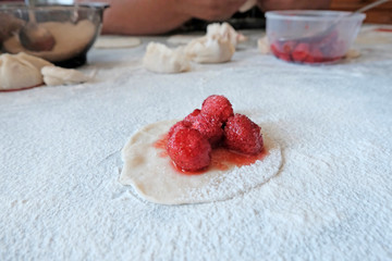 The concept of cooking dough. The rolled out circle of dough with filling in the middle of the strawberries. The background of scattered flour, raw pieces of dough next.Dumplings with berries.