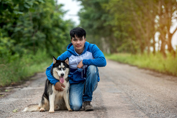 Man and dog Siberian huskies concept. Asian young man with his dog sitting on street in the park.