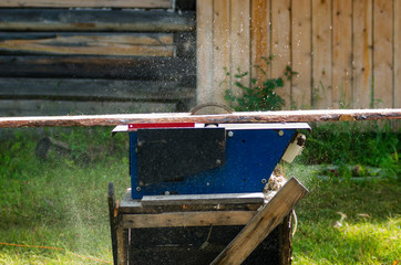 A rapidly spinning circular saw blade on the desktop cuts a pine Board with chips and sawdust...